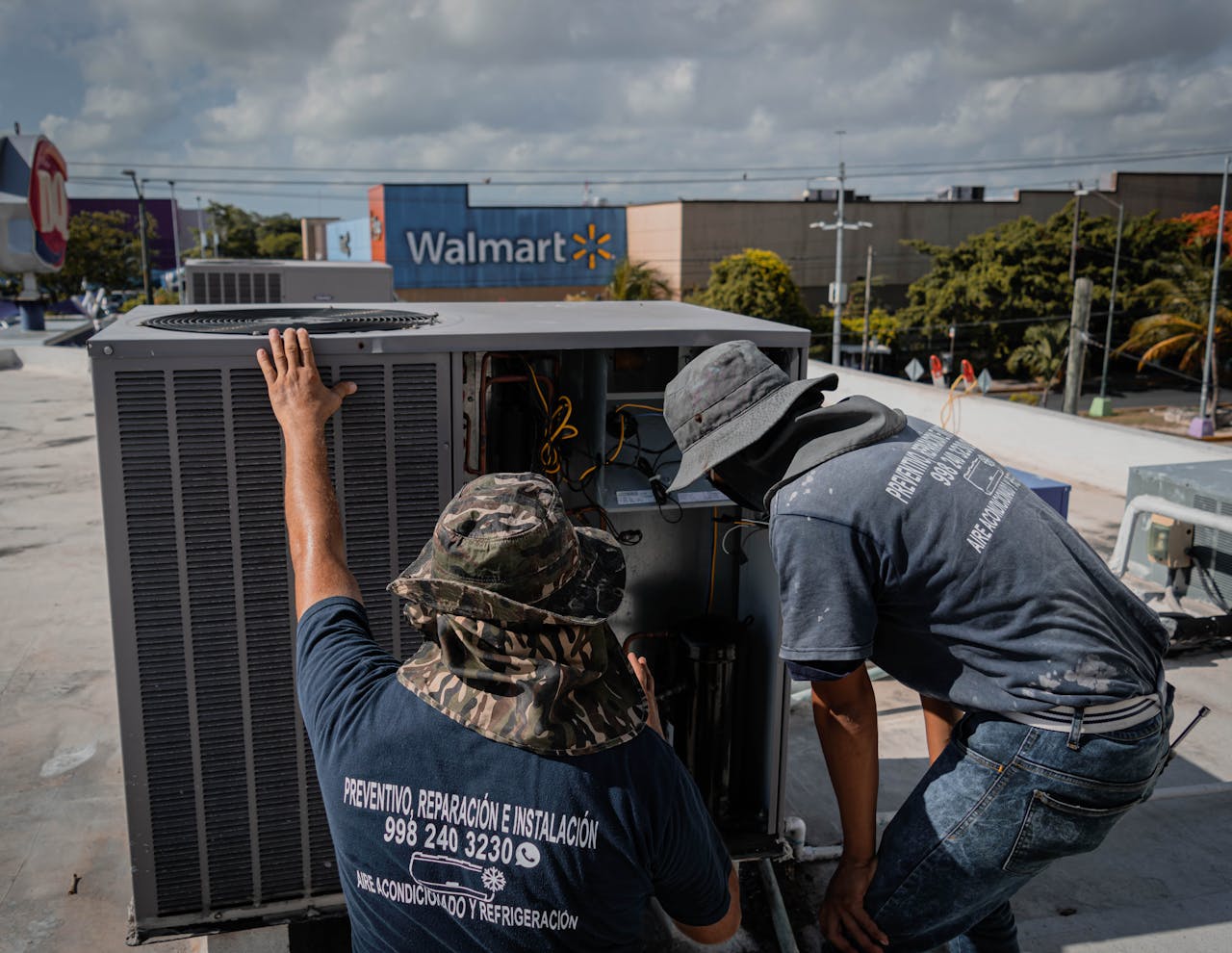 Men Wearing Hats Looking at the Outside Unit of an Air Conditioner at the Rooftop